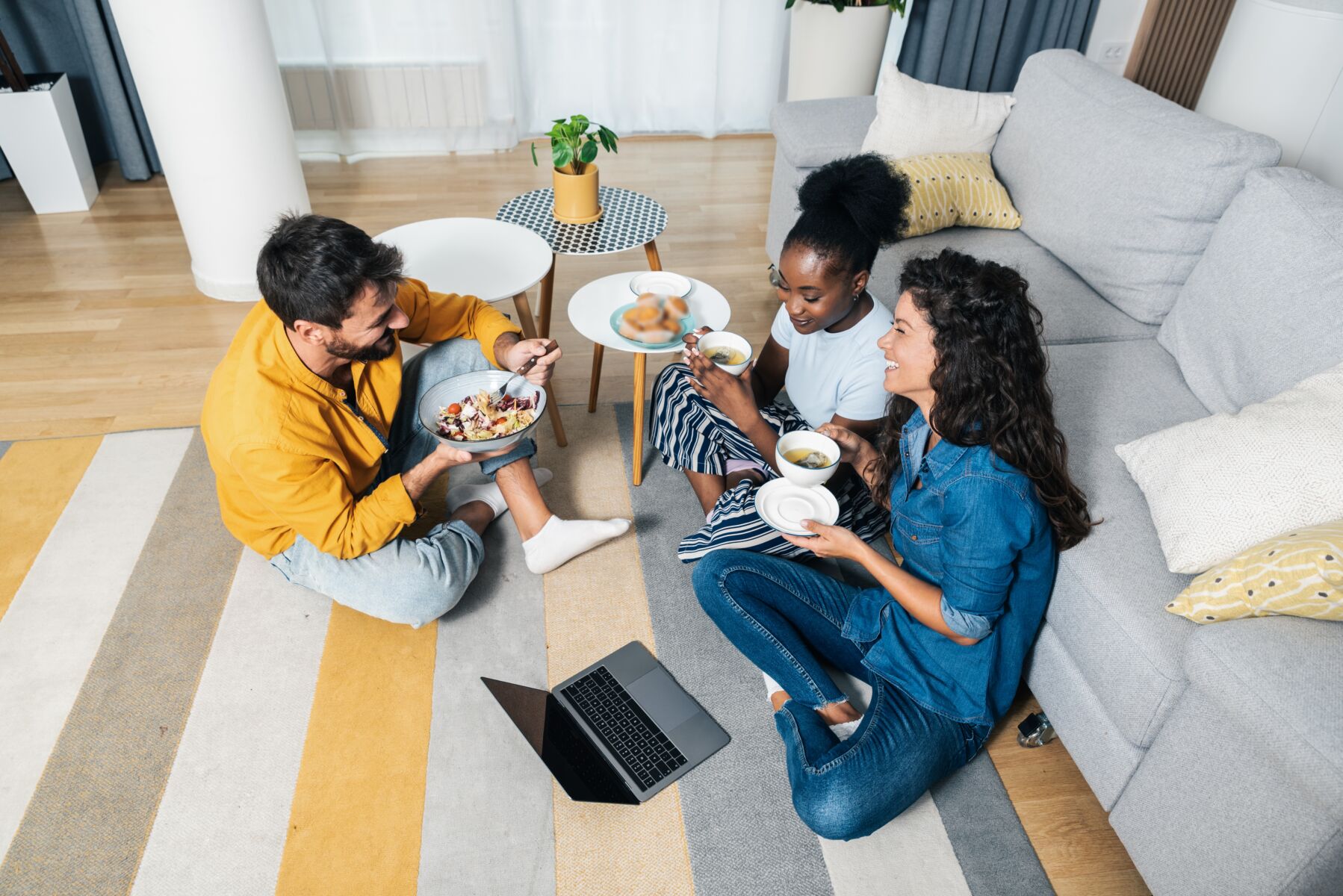 A group of friends sit on the floor and eat a meal.