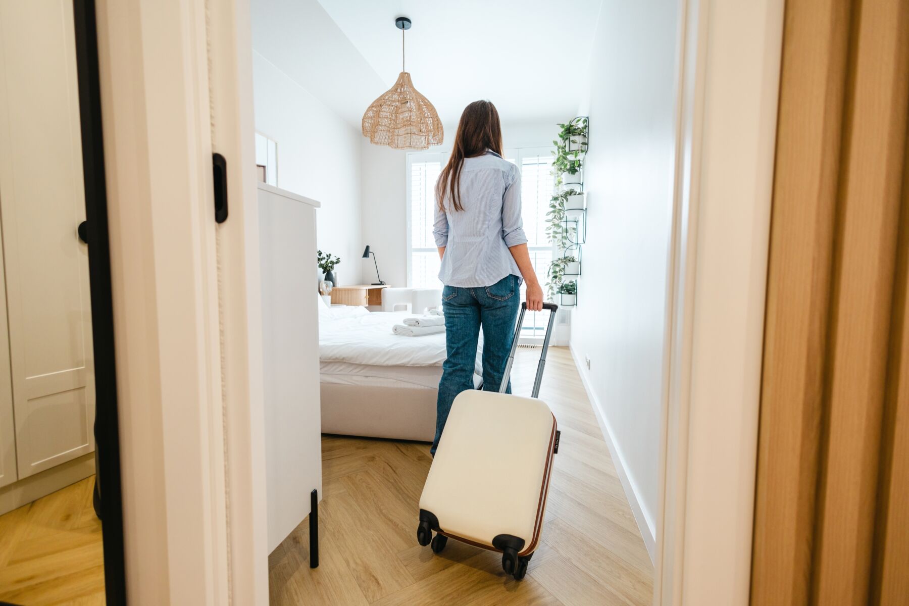 A woman with a suitcase walks into a furnished room.