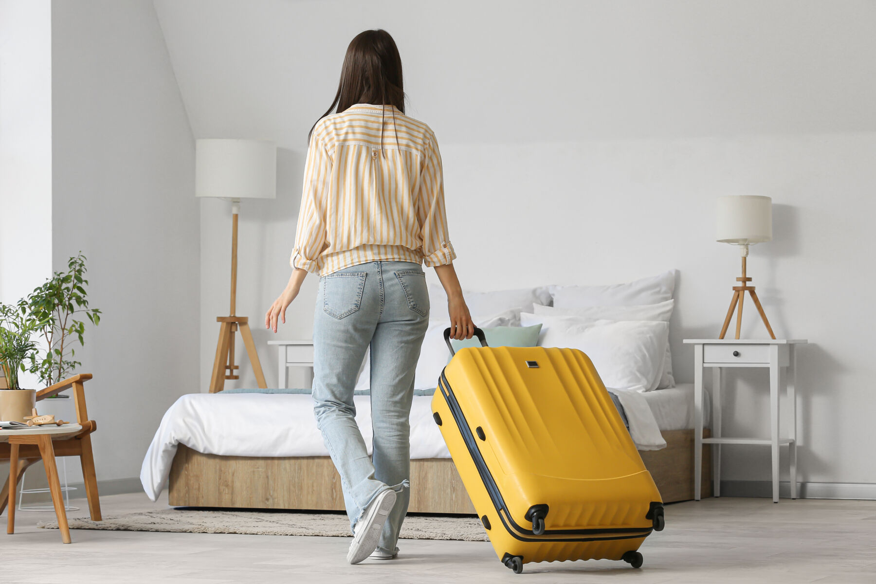 Photo shows back view of woman with suitcase in light coliving room.