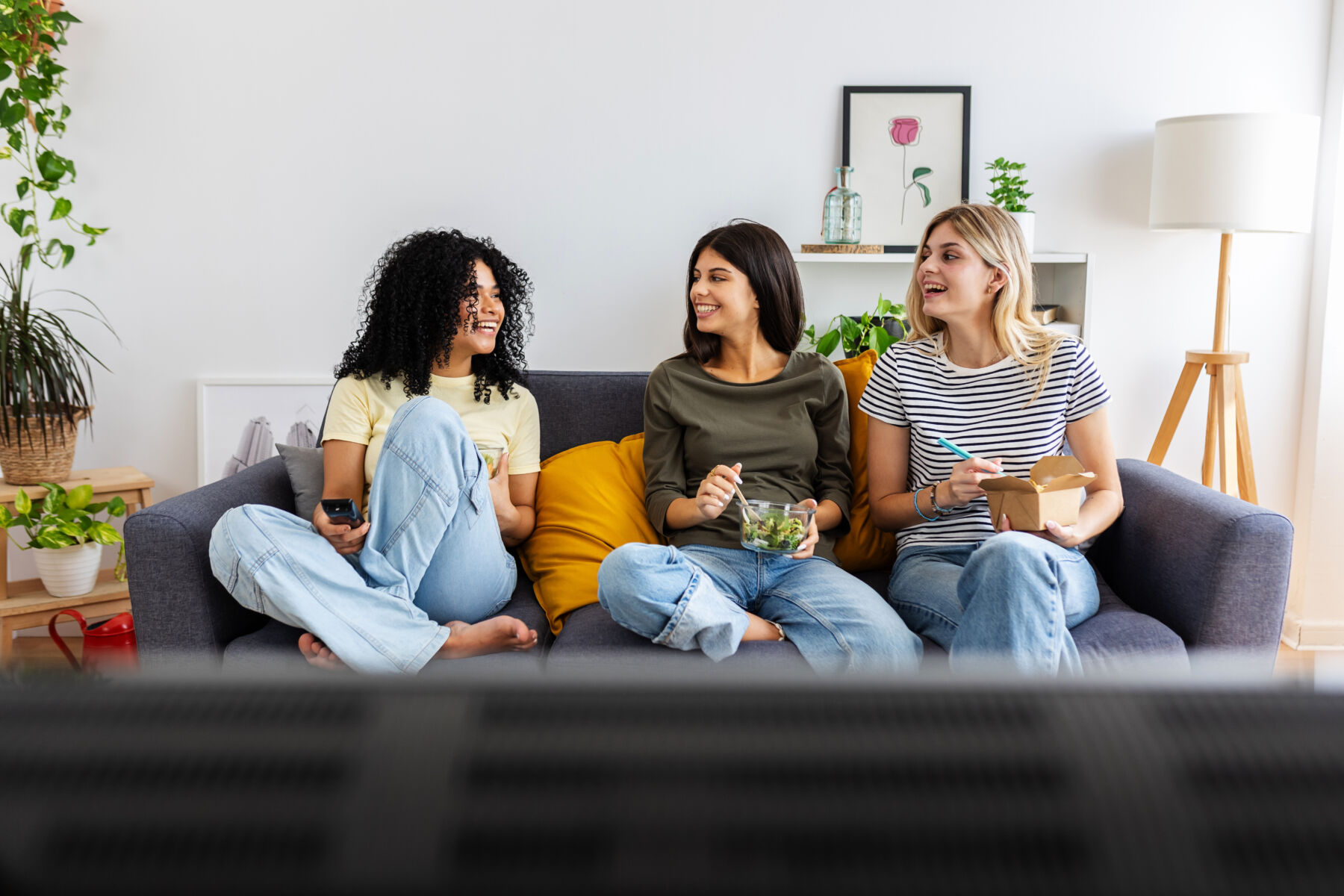 Photo shows three happy college female students working together on laptop at home. Millennial student flatmate friends enjoying time together at shared apartment.