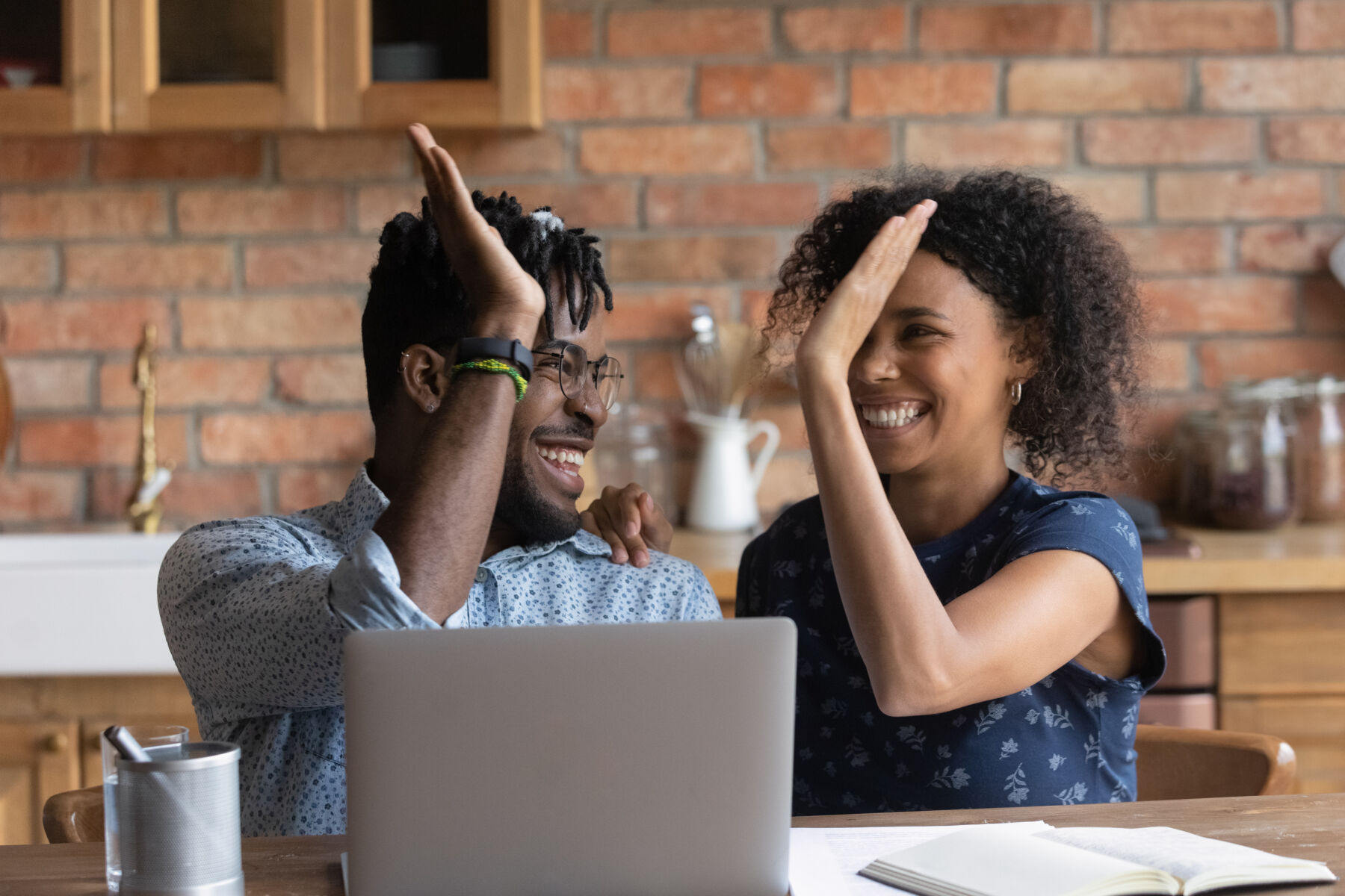 A young African American couple high-five in front of a laptop.