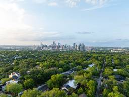Aerial perspective of Austin, Texas skyline emerging above a verdant tree cover in a residential area.