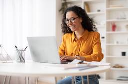 A woman with an orange shirt sits at a laptop.