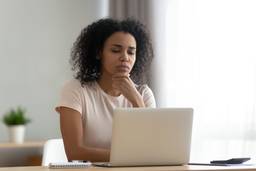 An African American woman looks pensive while using her laptop.