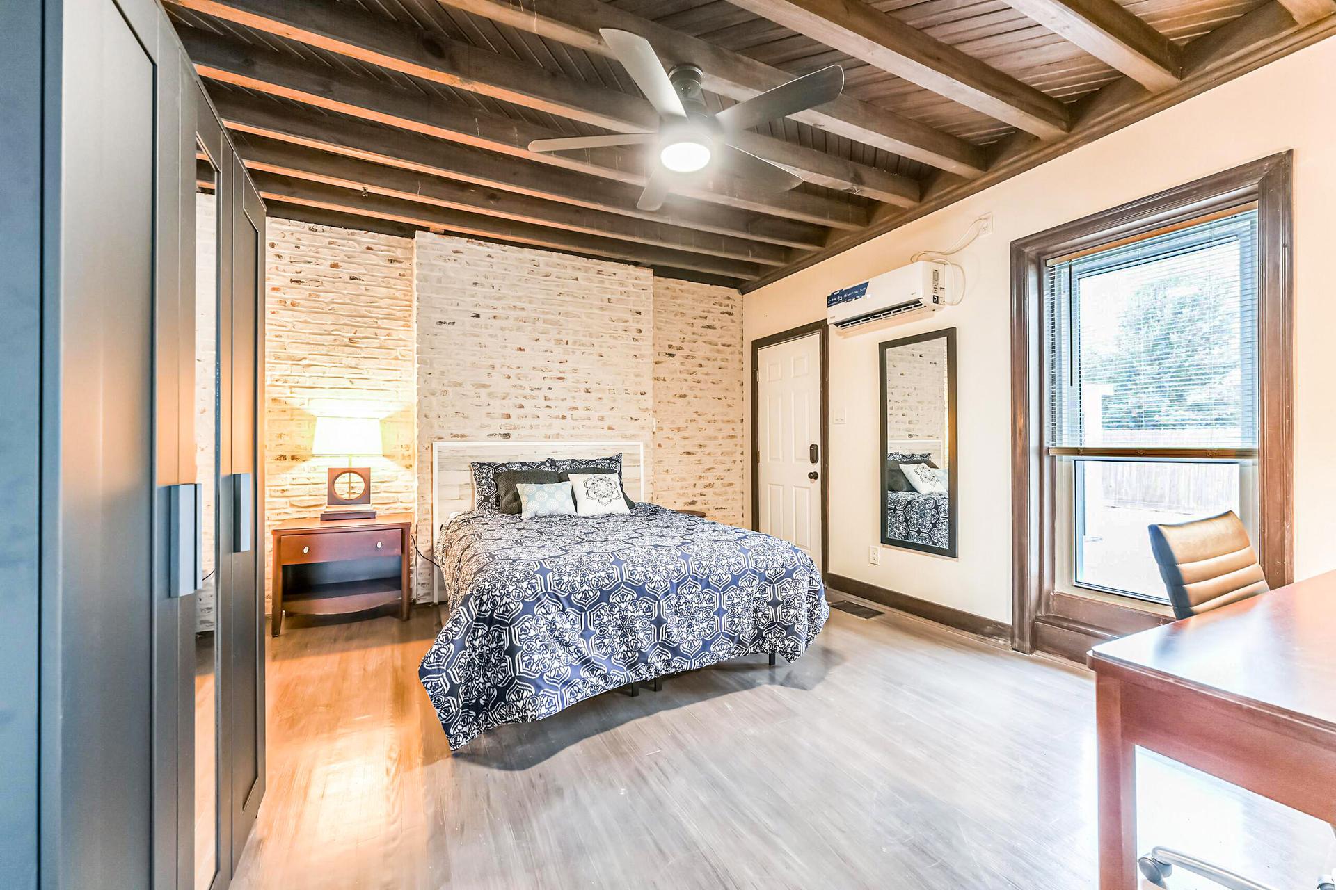 Large room with minisplit AC, queen bed, hybrid mattress, night stand, full length mirror, and desk with chair.