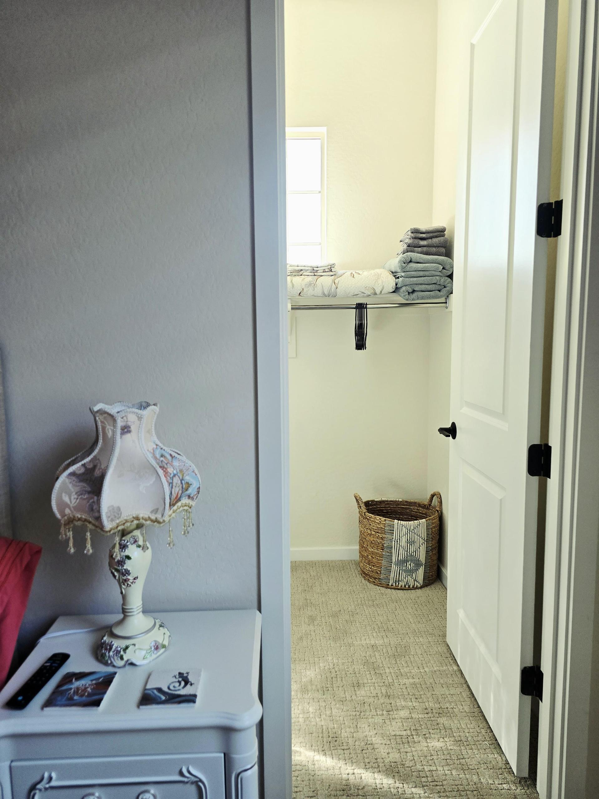 Walk-in closet with shelves, hangers, fresh linens, laundry basket, and soft natural light from a small window. Neat & serene