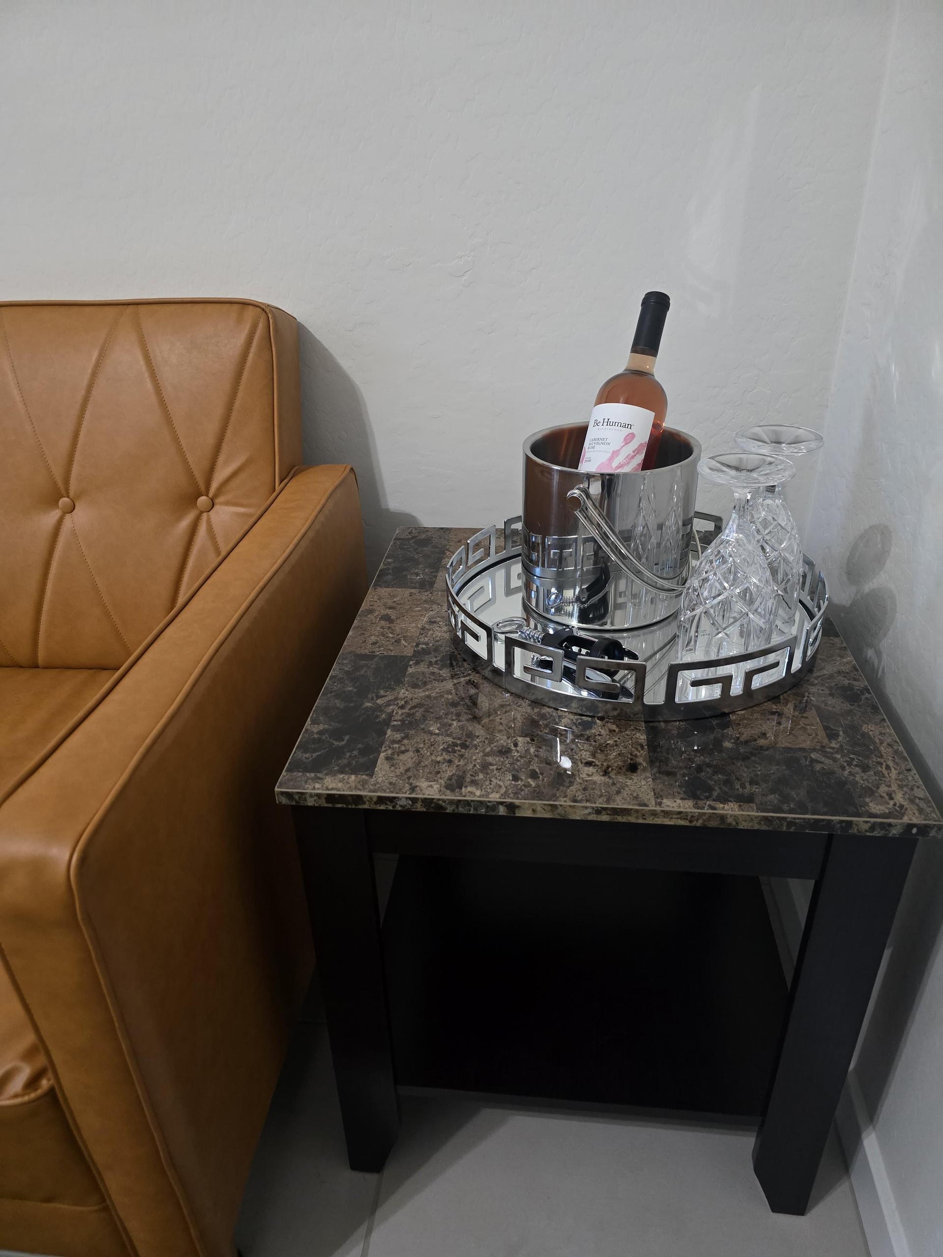 A marble-top side table holds a silver tray with a wine chiller, one bottle of complimentary wine, glasses, and opener.