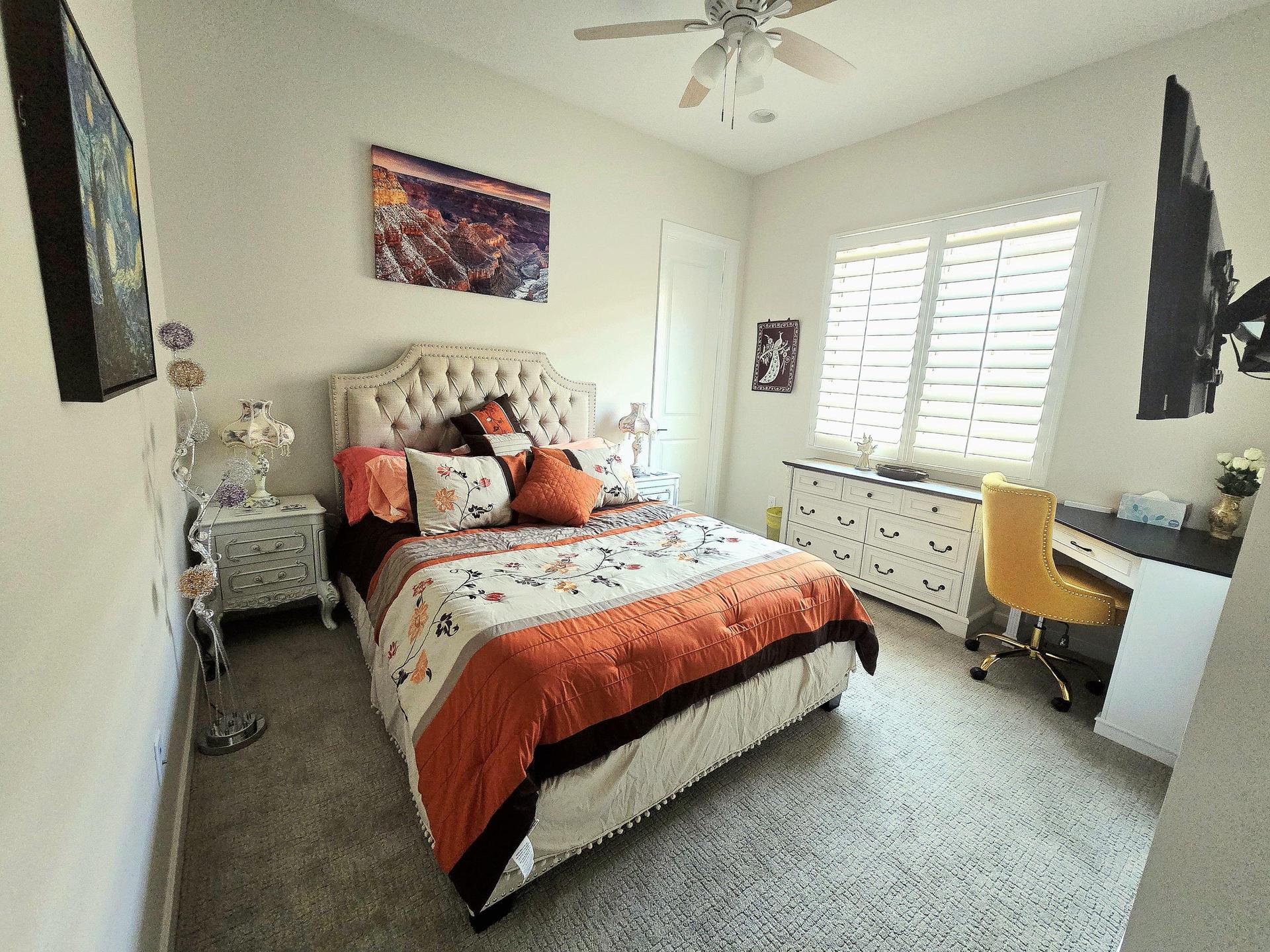 Beautiful room with queen bed, tufted headboard, big smart TV, dresser, and a workspace desk with sandstone-colored chair.