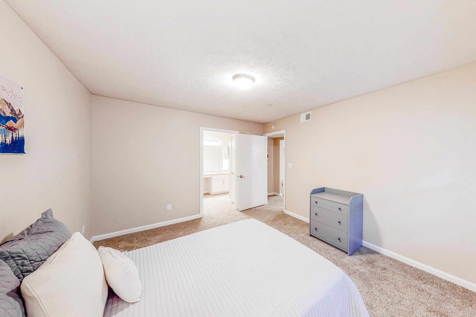 Gorgeous master suite equipped with a private bathroom, natural daylight, a queen bed, nightstand, vintage lamp and dresser.