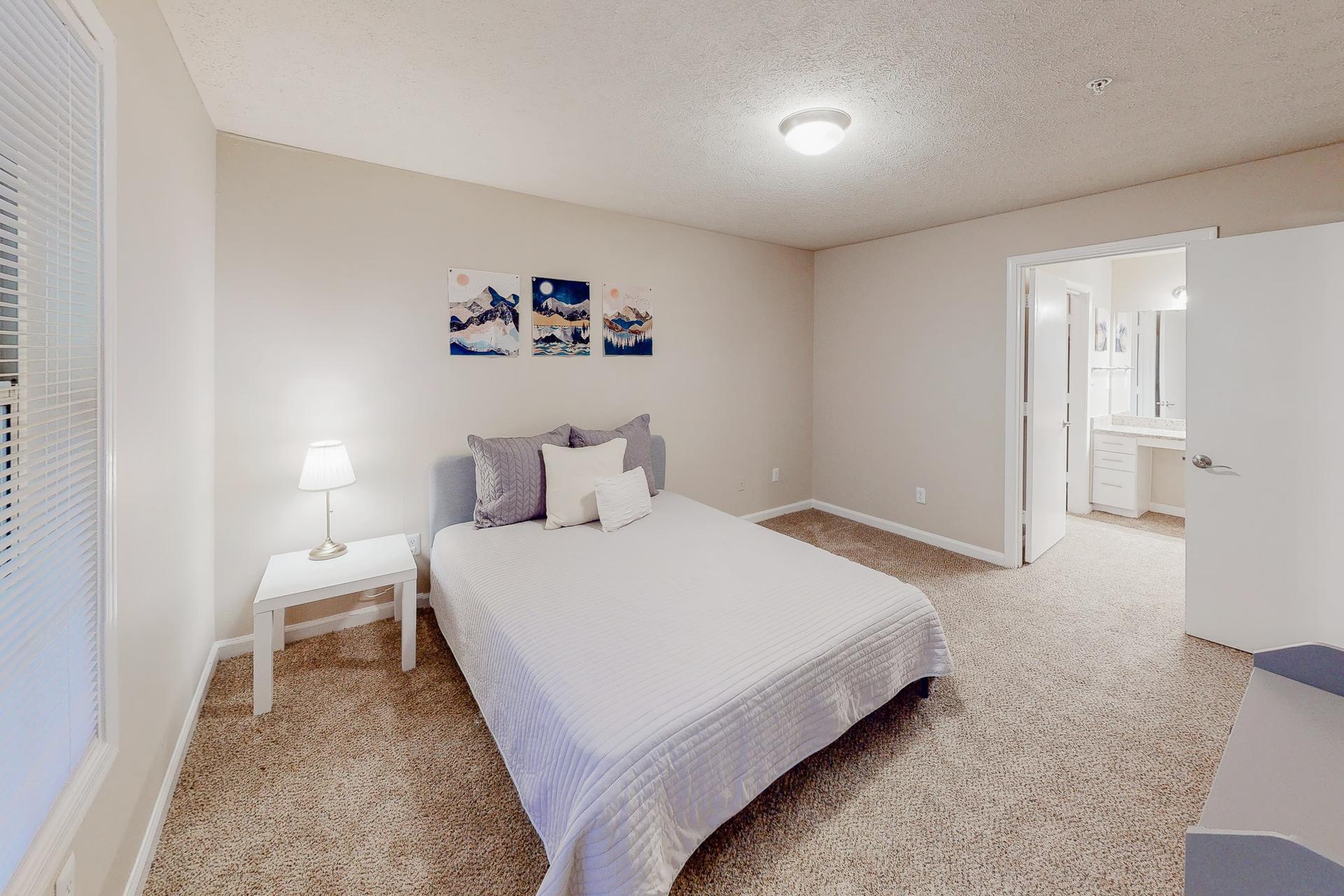 Gorgeous master suite equipped with a private bathroom, natural daylight, a queen bed, nightstand, vintage lamp and dresser.
