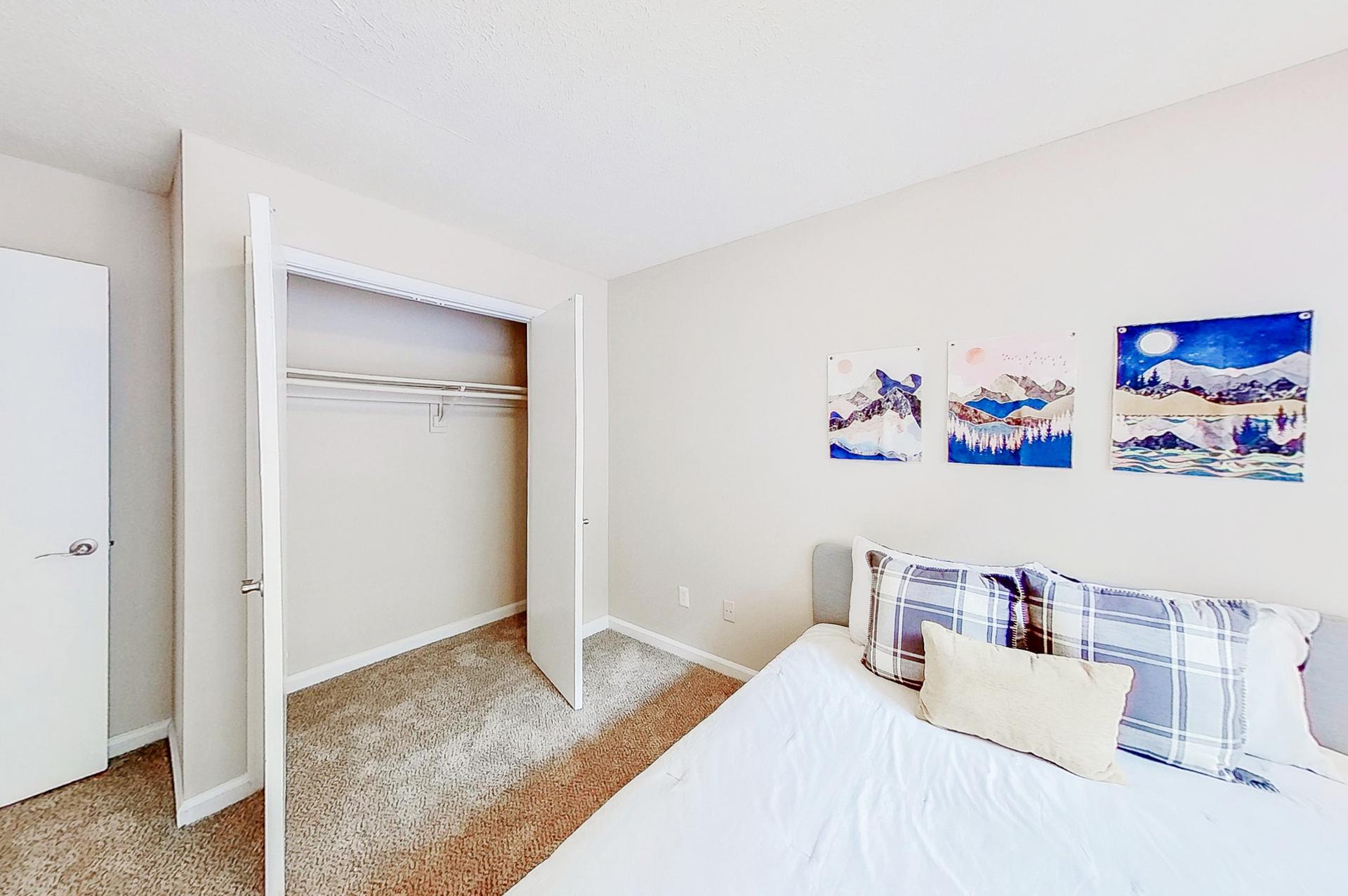 Cozy room equipped with a queen bed, night stand, vintage lamp, dresser and a reach-in closet.