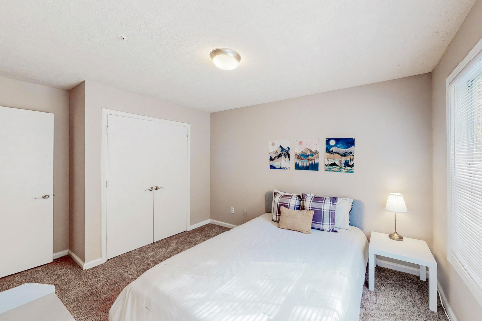 Cozy room equipped with a queen bed, night stand, vintage lamp, dresser and a reach-in closet.