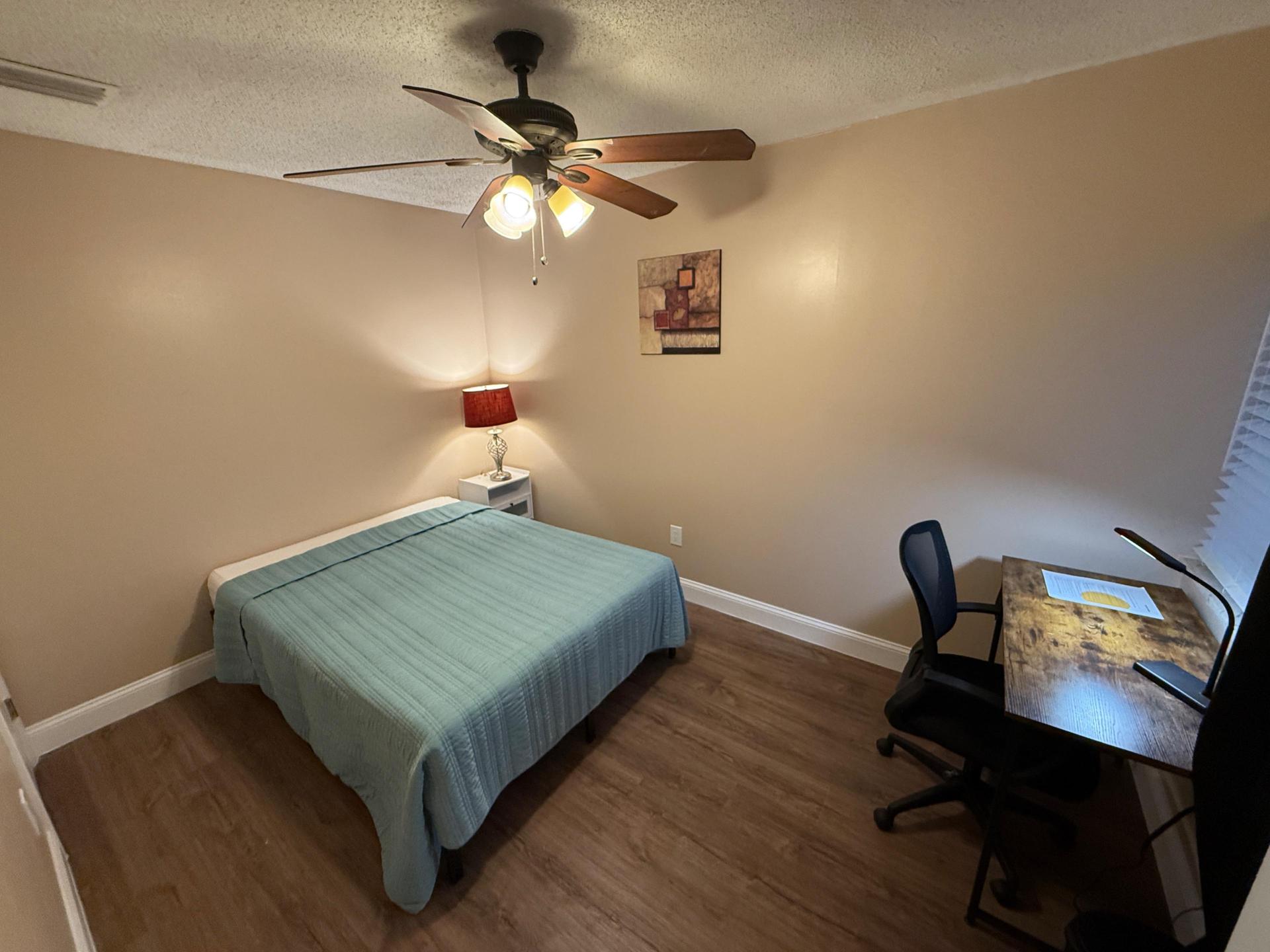 Full size bed with end table and light as well as a desk, office chair and lamp