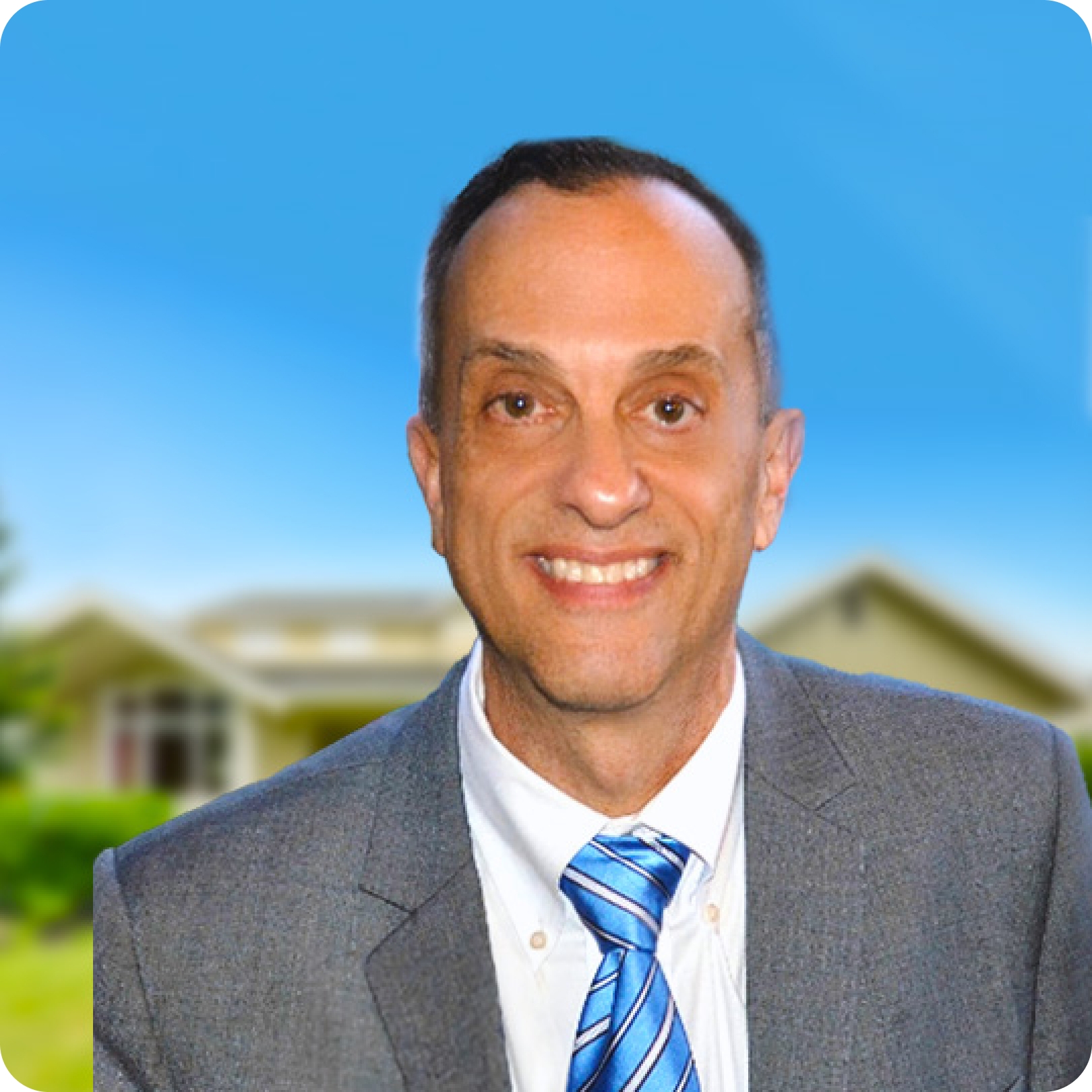 An older man in a suit smiles and has a house behind him