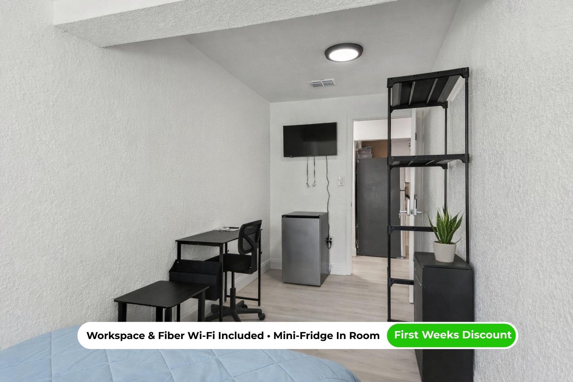 Spacious angle highlights desk setup, shelving and Smart TV, with mini fridge, central A/C, and comfy queen bed.