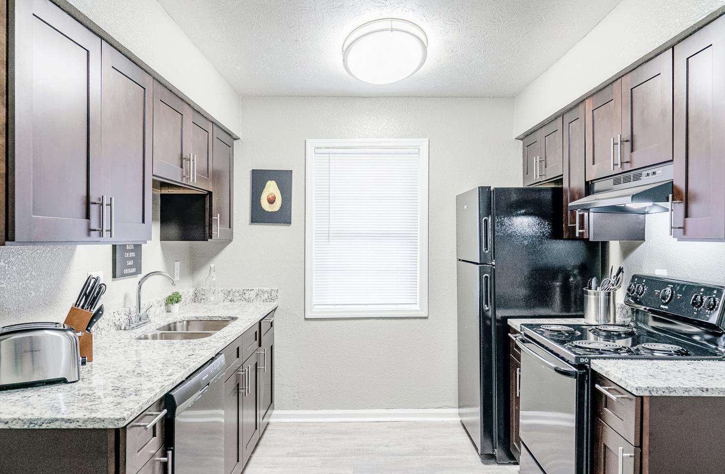 Gorgeous kitchen with granite countertops, cookware, toaster, utensils, and black appliances.