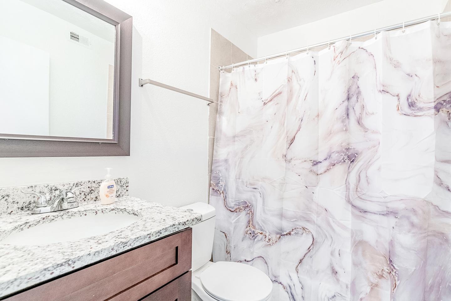 Spacious shared bathroom featuring commode, tub/shower combo and granite countertops.